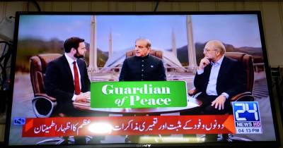 O vice-presidente dos Estados Unidos, JD Vance, com o primeiro-ministro paquistanês, Shehbaz Sharif, e o presidente do parlamento iraniano, Mohammad Bagher Ghalibaf (à direita), aparecem num ecrã de televisão durante as negociações EUA-Irã, em Peshawar, Paquistão.